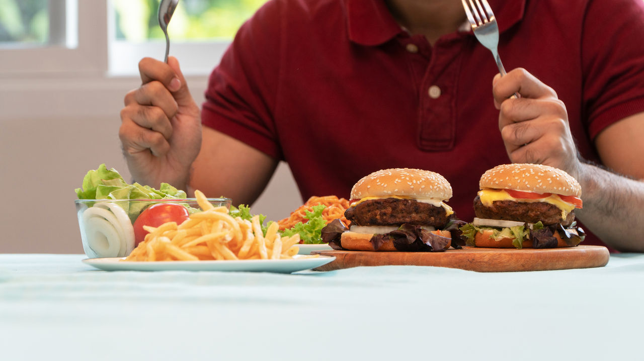 Young Man holding knife and fork are ready to eating a hamburger, French fries, and Spaghetti for Lunch. Concept of binge eating disorder (BED) and Relaxing with Eating junk food and unhealthy foods. Young Man holding knife and fork are ready to eating a hamburger, French fries, and Spaghetti for Lunch. Concept of binge eating disorder (BED) and Relaxing with Eating junk food and unhealthy foods.